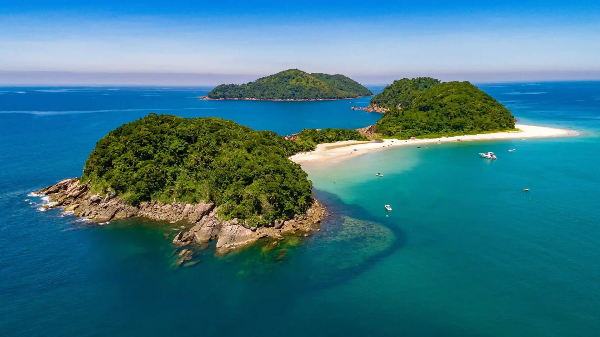 Vista aérea de As Ilhas na Praia da Barra do Sahy, São Sebastião - SP, com praia de areia branca, barcos ancorados e piscinas naturais de água cristalina