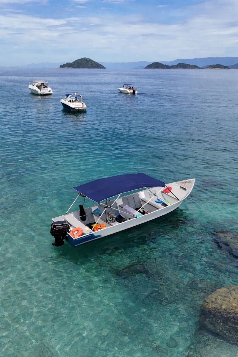 Barco com toldo azul ancorado em água transparente nas ilhas da Barra do Sahy